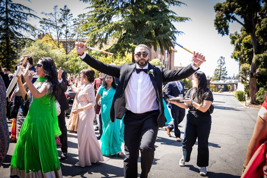 Man in tuxedo dances arms wide in procession