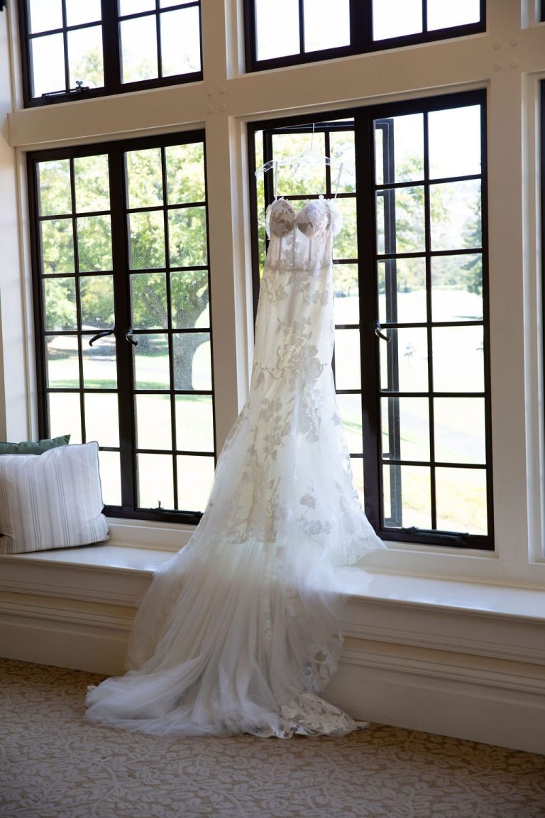 Full length wedding gown hanging in bright arched window