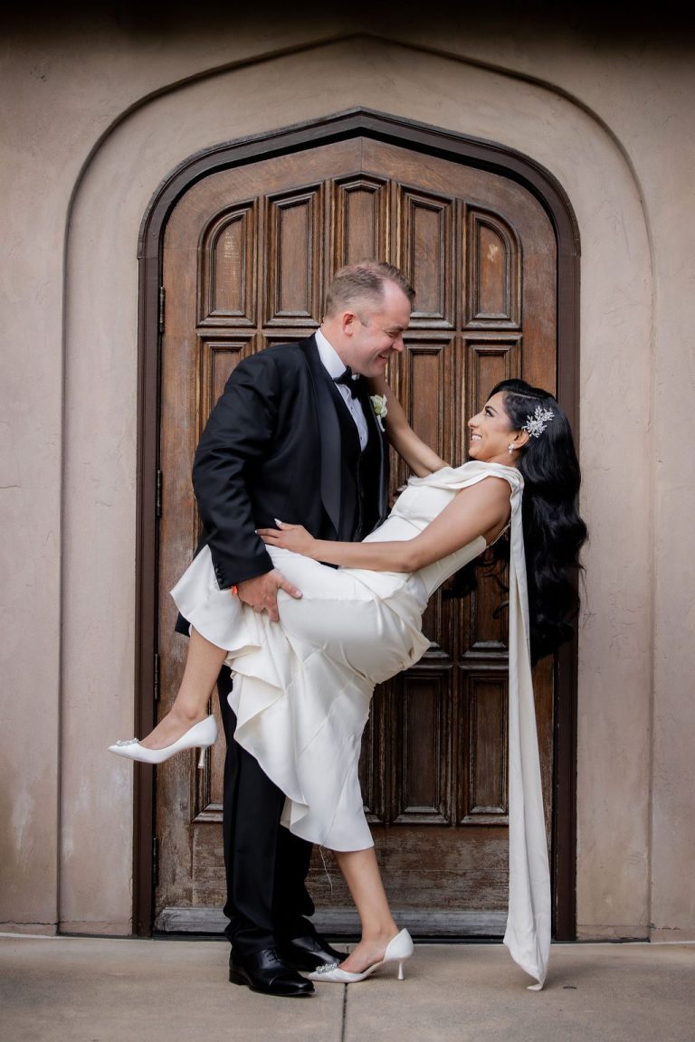 Groom lifting bride playfully before arched wooden door