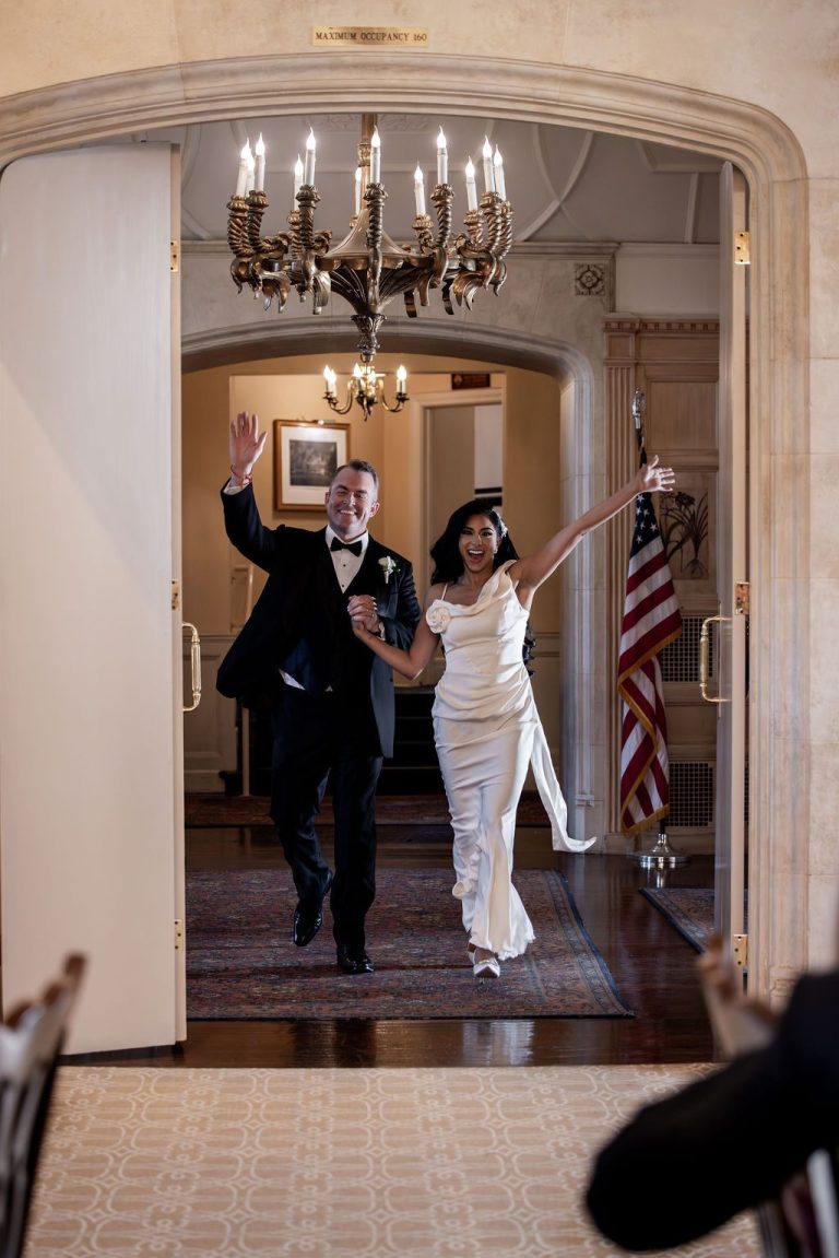 Couple entering reception under chandelier, guests reaching out