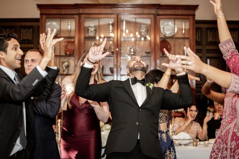 Groom dancing with arms outstretched among cheering guests