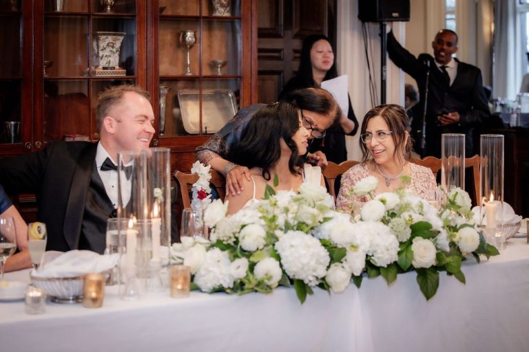 Wedding party laughing at head table with florals