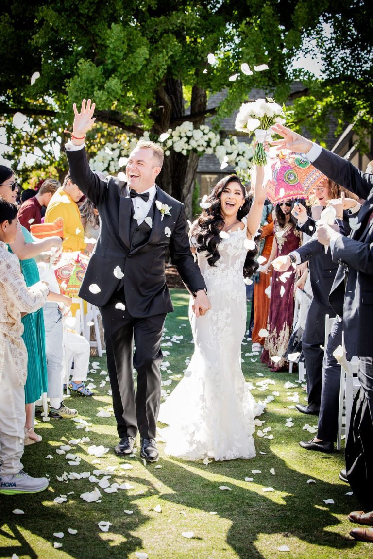 Couple exits under petal and confetti toss, guests cheering