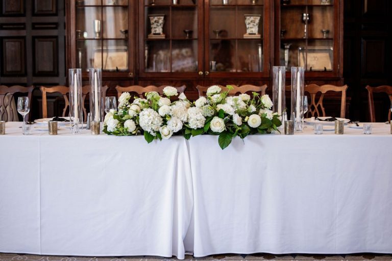 Long head table with white floral runner and candles