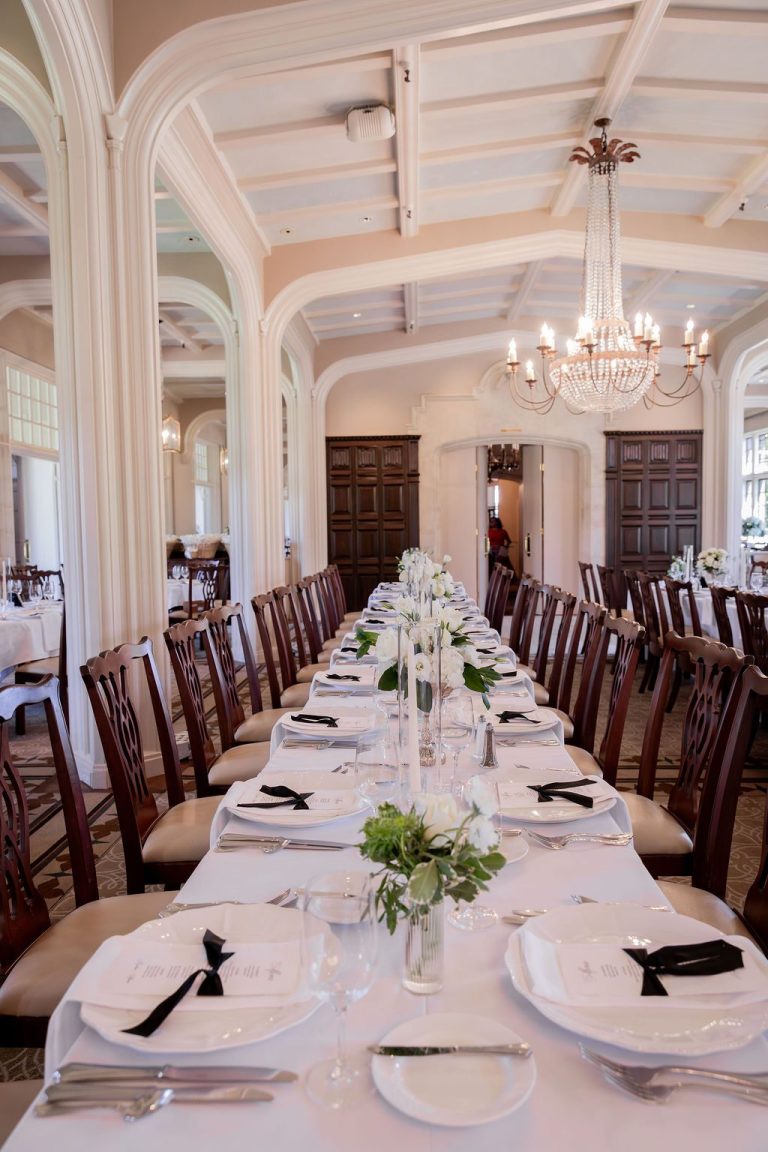 Long banquet table set with white linens and greenery