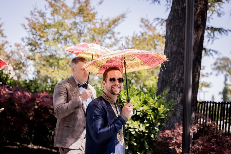 Two men holding decorative parasols under trees