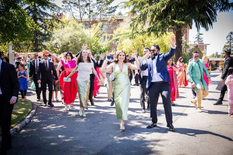 Couple and party walk arms raised through procession