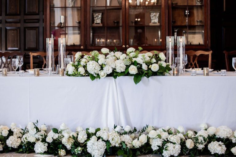 Head table draped with white florals and candles