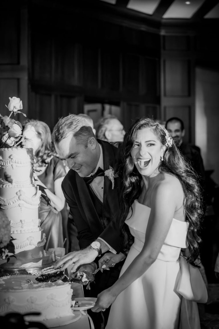 Bride laughing joyfully while cutting cake with groom