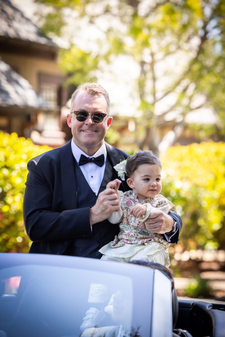 Man in tuxedo clapping with child by floral car