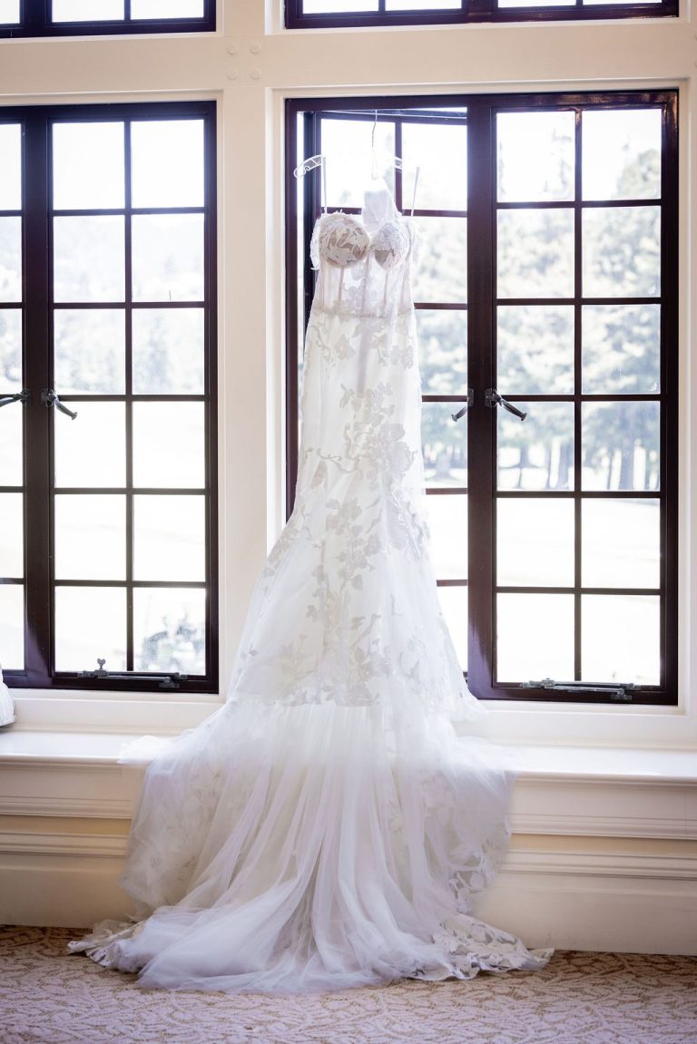 Wedding gown hanging in tall leaded window with lawn view