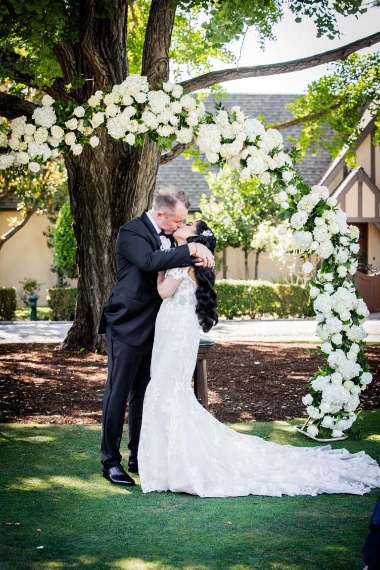 Couple kissing under floral arch surrounded by greenery