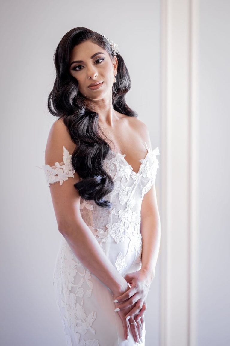 Radiant bride with long curls clasping hands, soft light