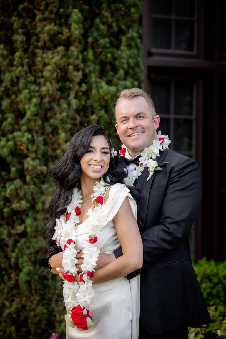 Bride and groom embracing before tall green hedge