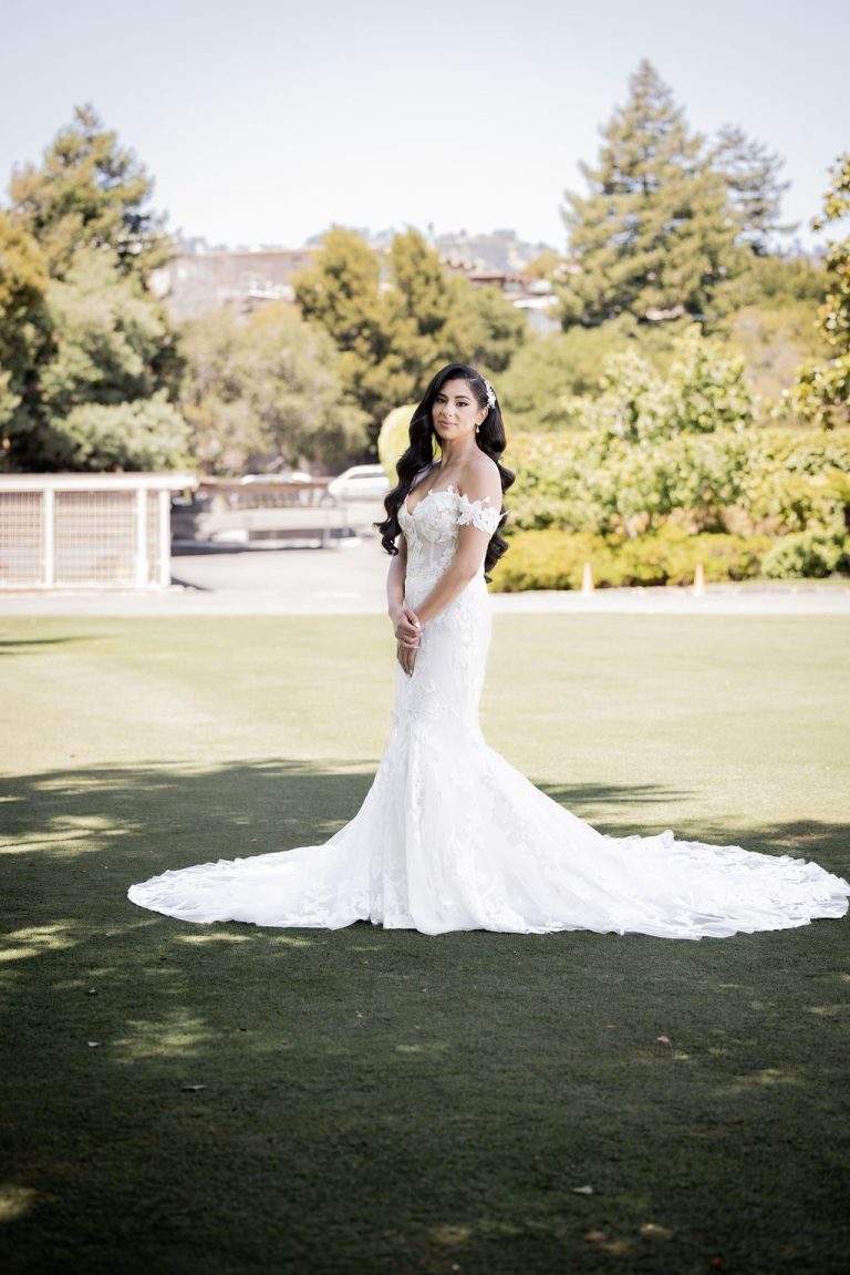 Bride with long train on green lawn with trees