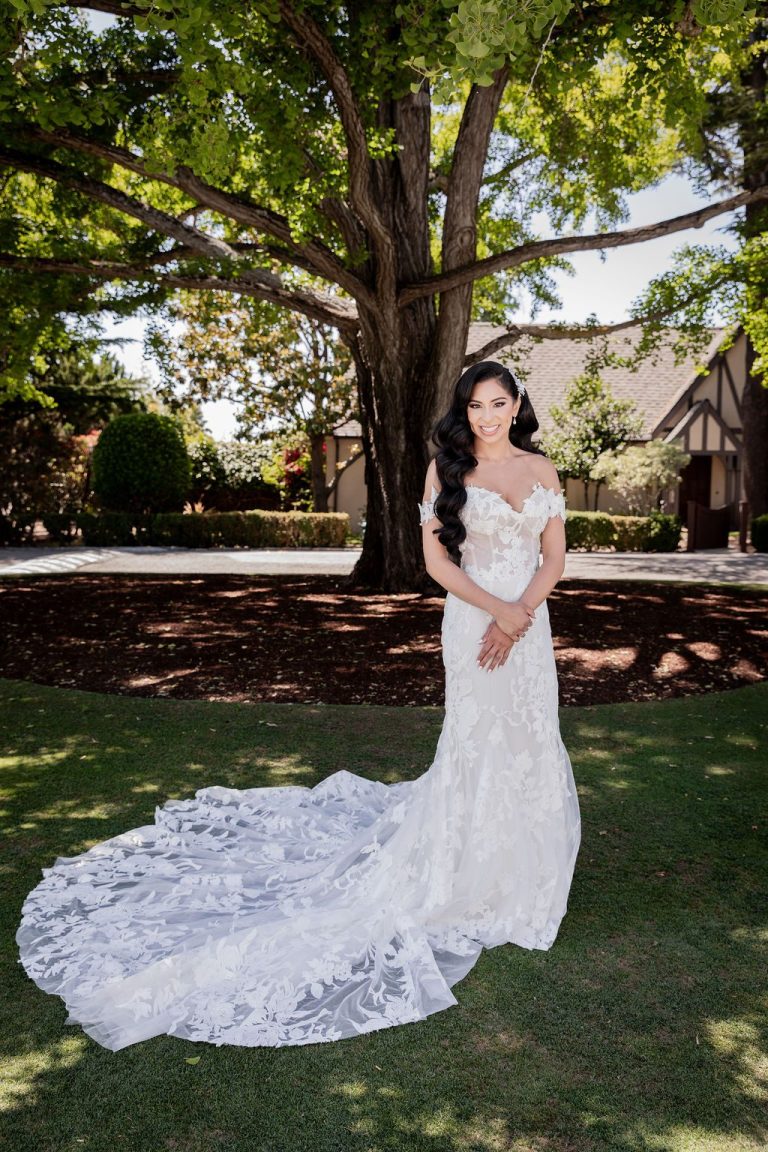 Bride solo showing long lace train under tree