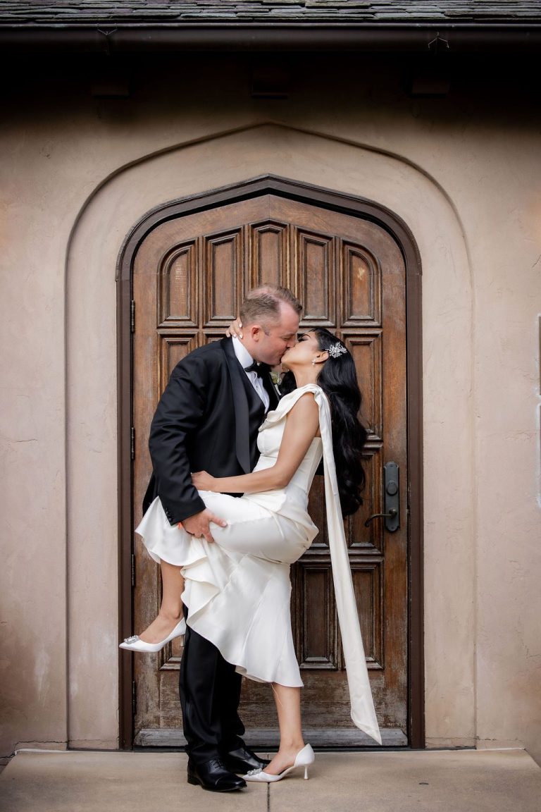 Groom dipping bride in kiss before arched wooden door