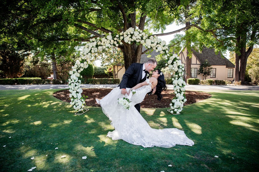 Groom dipping bride on lawn by floral arch
