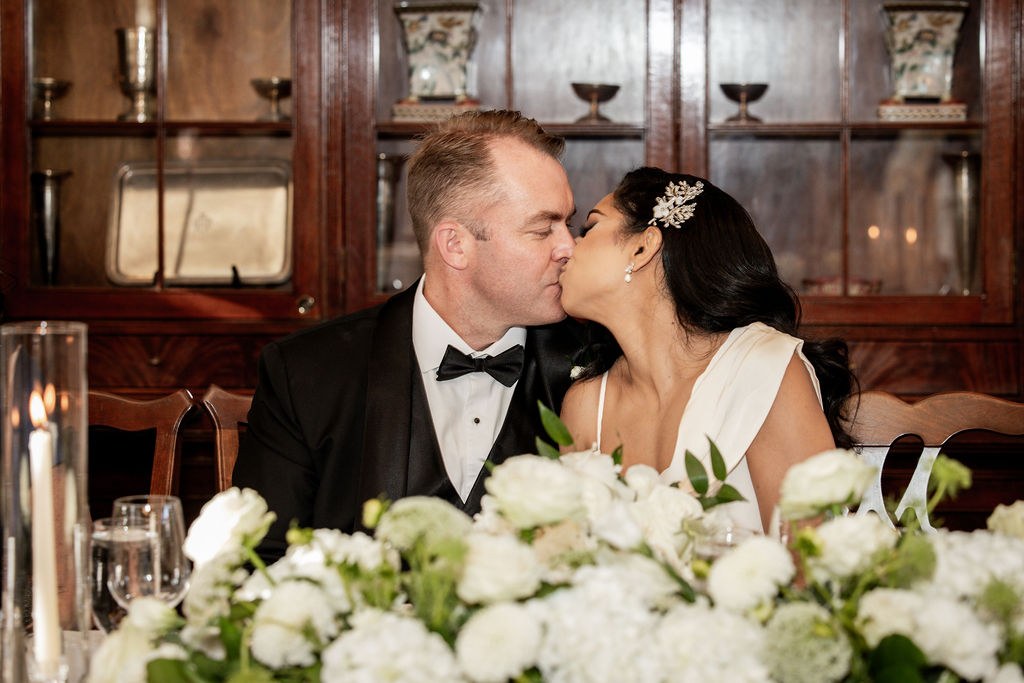 Bride and groom kissing at head table with florals