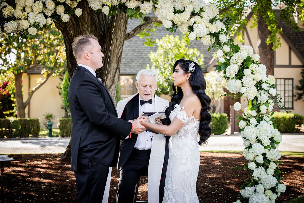 Couple holding hands under trees during outdoor vows