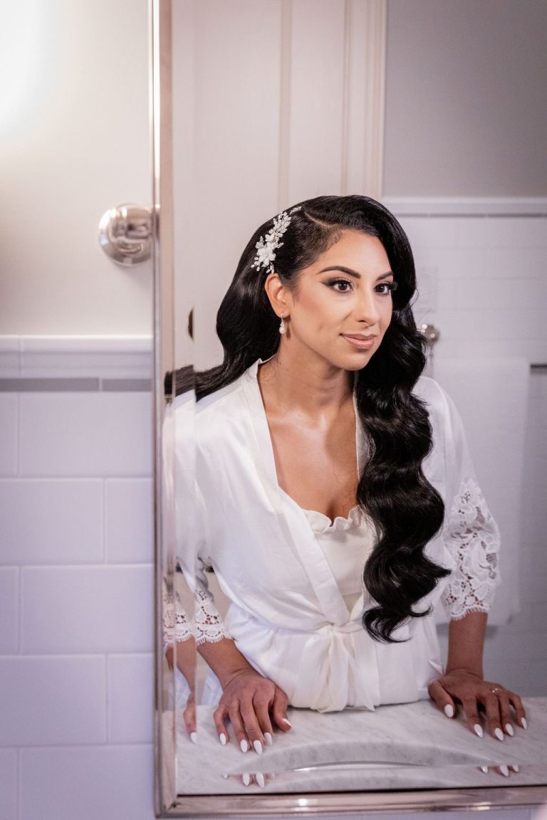 Bride in white robe leaning at mirror during prep