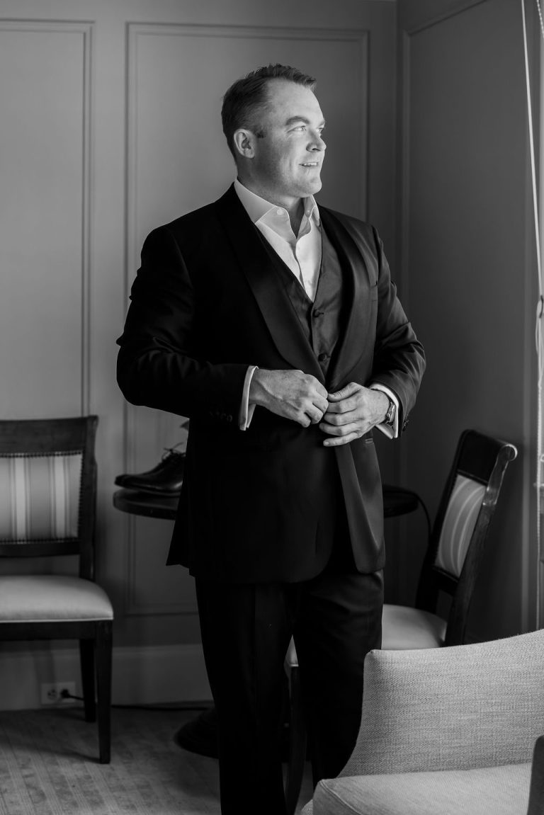 Black and white groom buttoning jacket looking away
