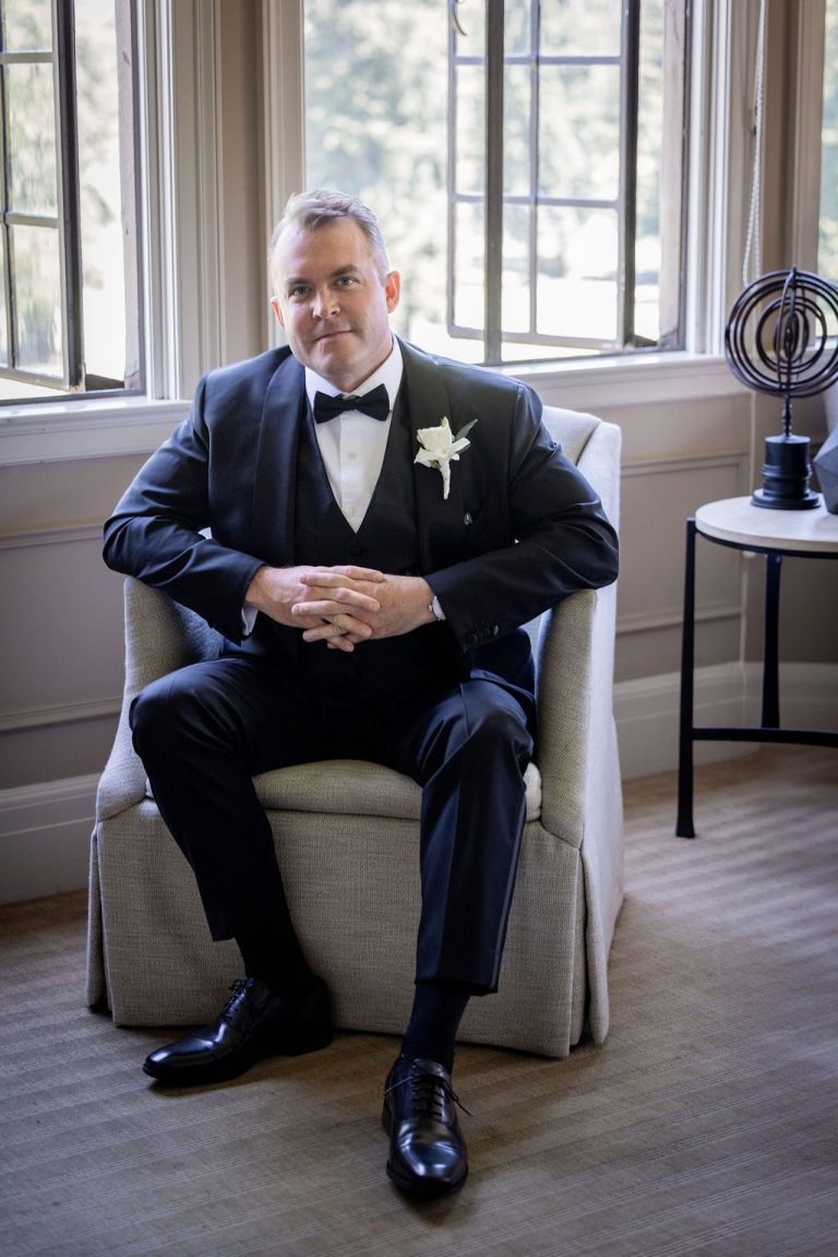 Groom seated in armchair hands clasped smiling