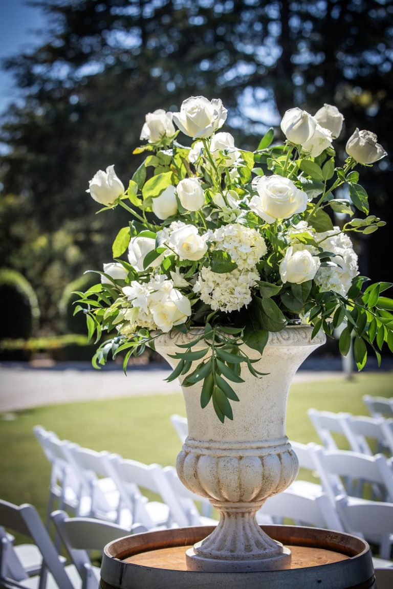 White rose floral urn beside ceremony chairs