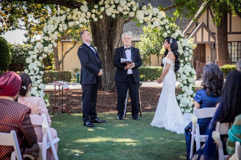 Couple exchange vows at floral arch with officiant