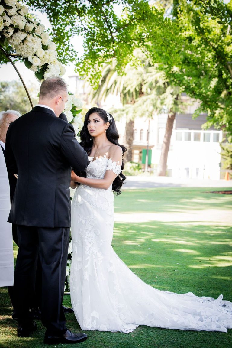 Bride and groom facing each other holding hands on lawn