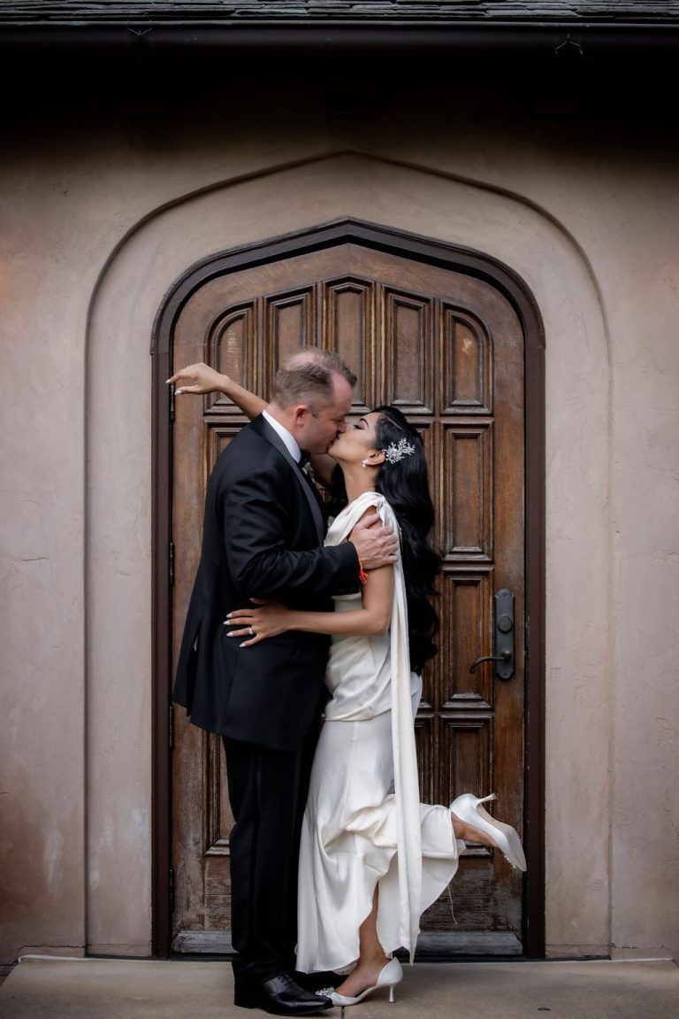 Bride lifting leg during kiss before arched door