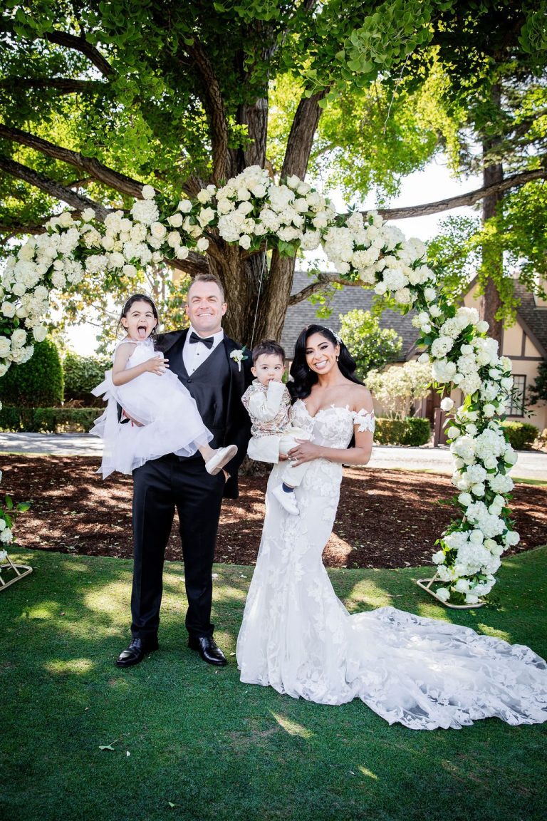 Couple with child pose at floral arch under tree