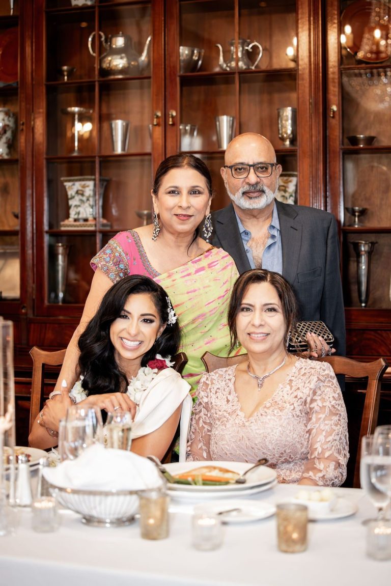 Bride seated with parents posing at reception table