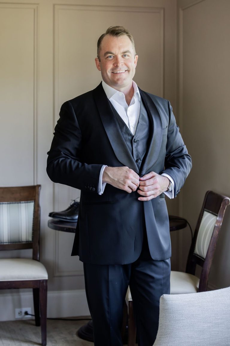 Groom buttoning jacket smiling near window