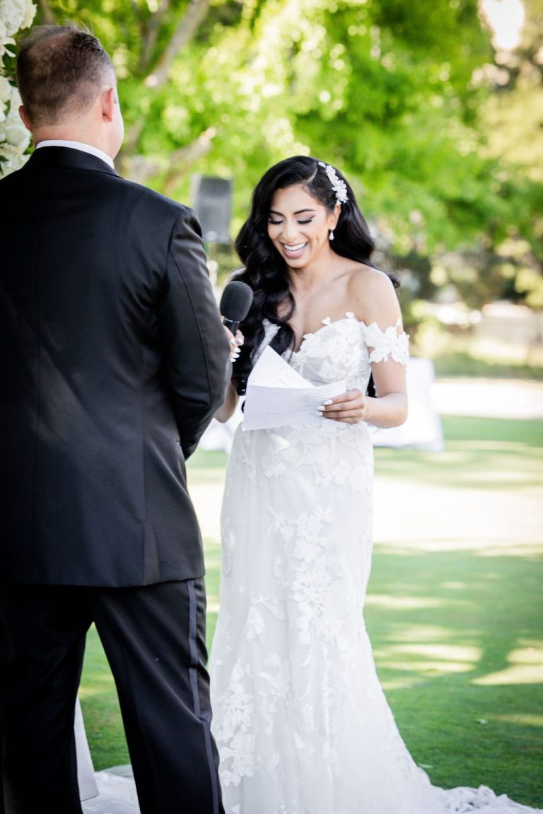 Bride reading vows from paper into microphone, groom watching