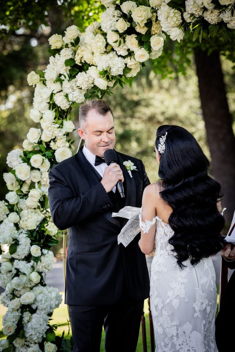 Groom emotional facing bride under white floral arch