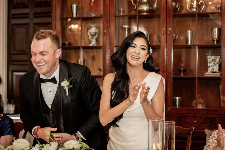 Bride clapping beside smiling groom at head table