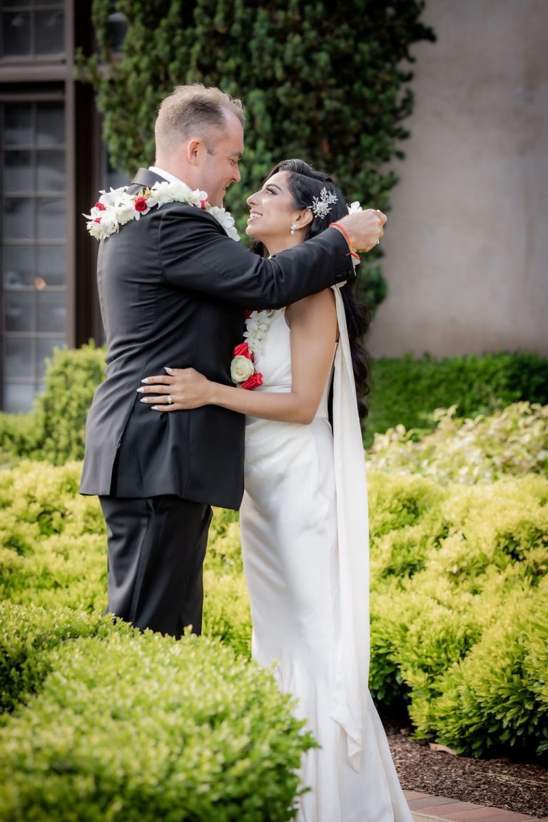 Bride and groom embrace among green hedges outdoors