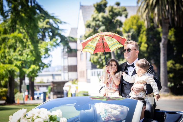 Man holding two children under red parasol in convertible