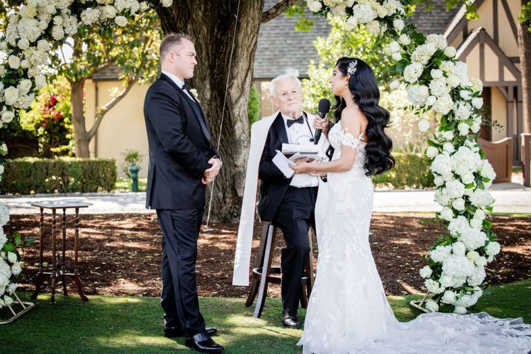 Couple exchanging vows under floral arch with officiant