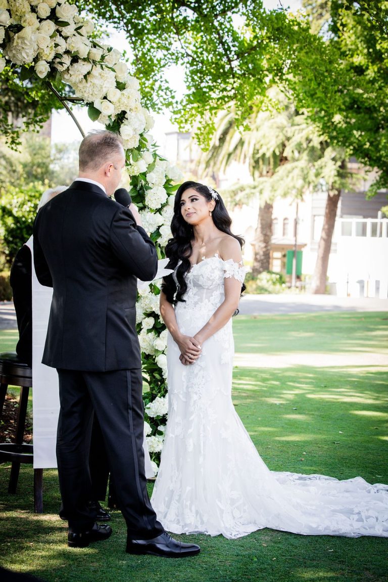 Bride gazing at groom holding hands under greenery