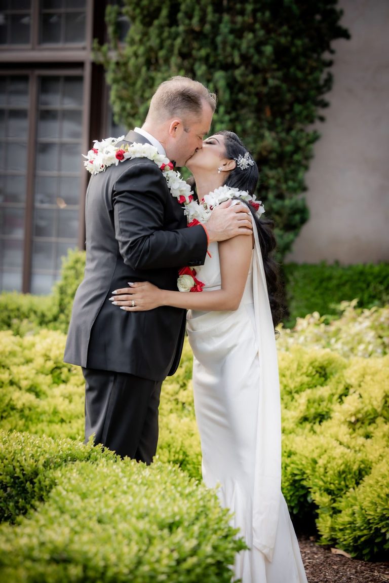 Groom kisses bride wearing red and white leis