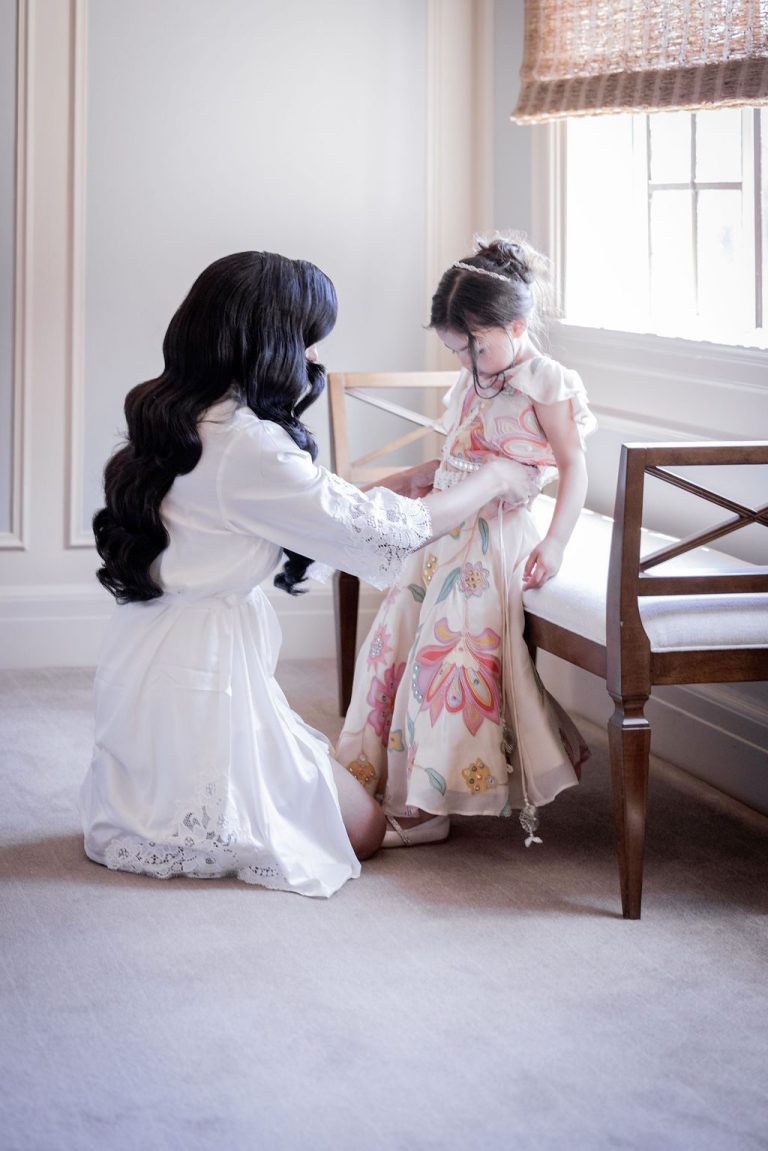 Bride helping young girl dress by sunlit window
