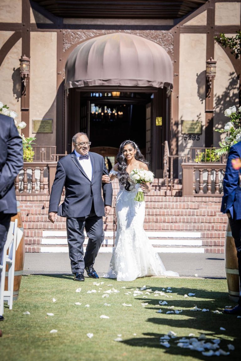 Bride and escort walking petal aisle with guests watching