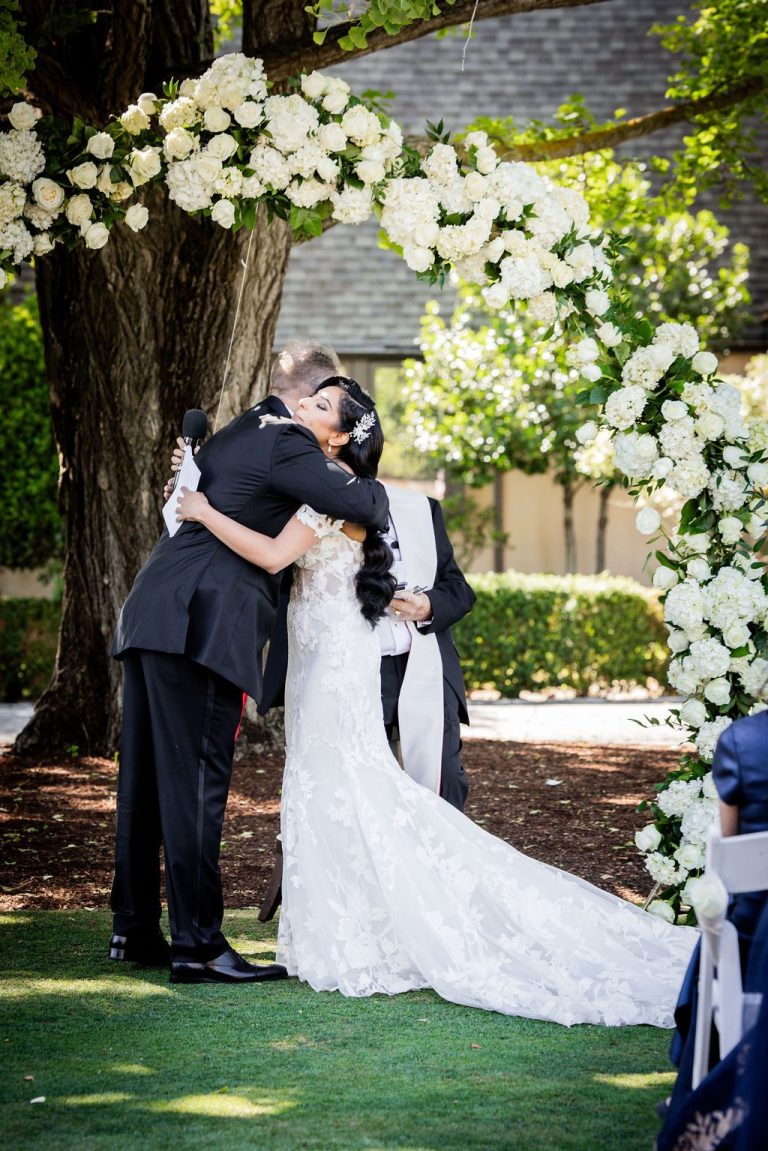 Bride and groom embracing during outdoor ceremony under trees
