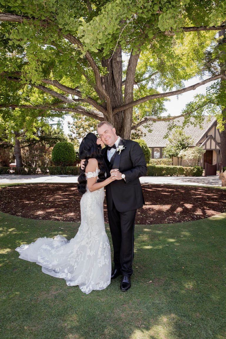 Groom dips and kisses bride on green lawn