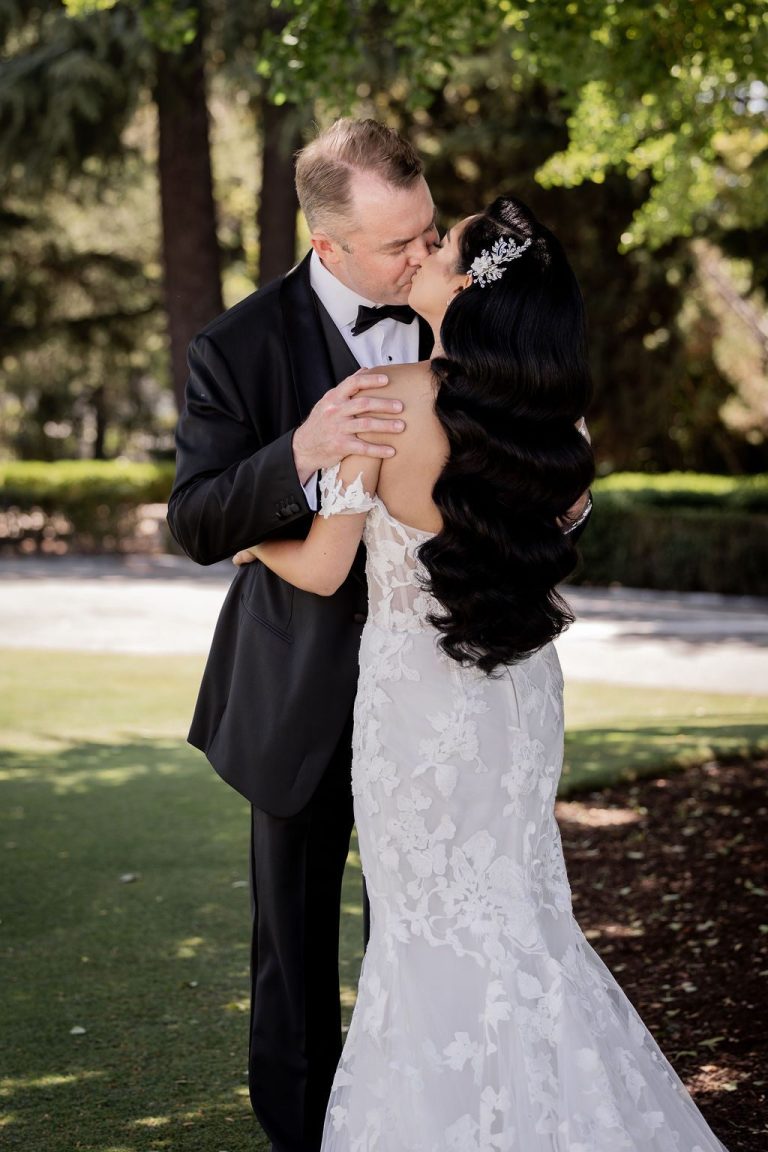 Groom kissing bride's forehead under shady trees