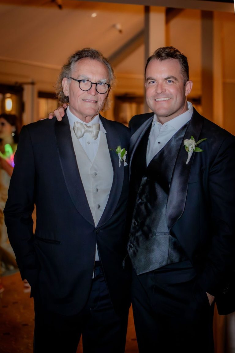 Two men in tuxedos posing together at reception
