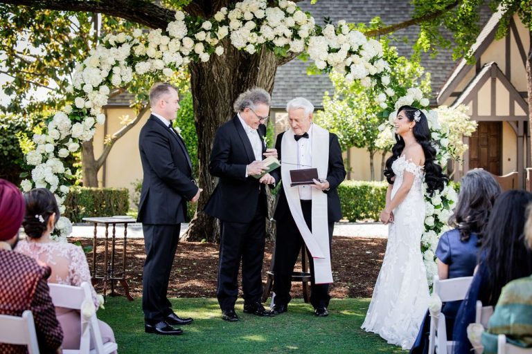 Groom, officiant, and bride at arch under tall tree
