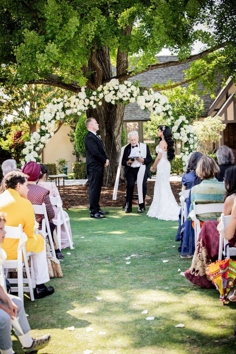 Aisle view of couple at floral arch with seated guests